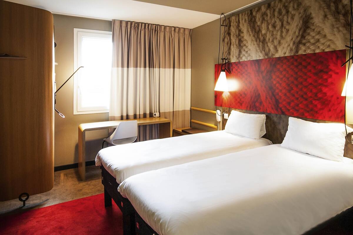 A hotel room with two beds, a desk, a chair, a telephone, and a window with curtains.