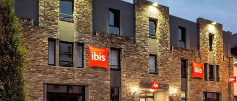 A hotel with stone facade, multiple windows, and red signage.