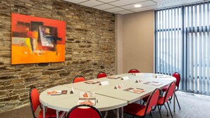 Una sala de conferències amb una paret de pedra, un ampli quadre abstracte i vista a través de persianes verticals.
