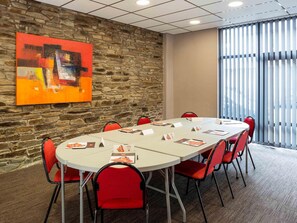 Un salón de conferencias con pared de piedra, un cuadro abstracto de gran tamaño y vistas a través de persianas verticales.