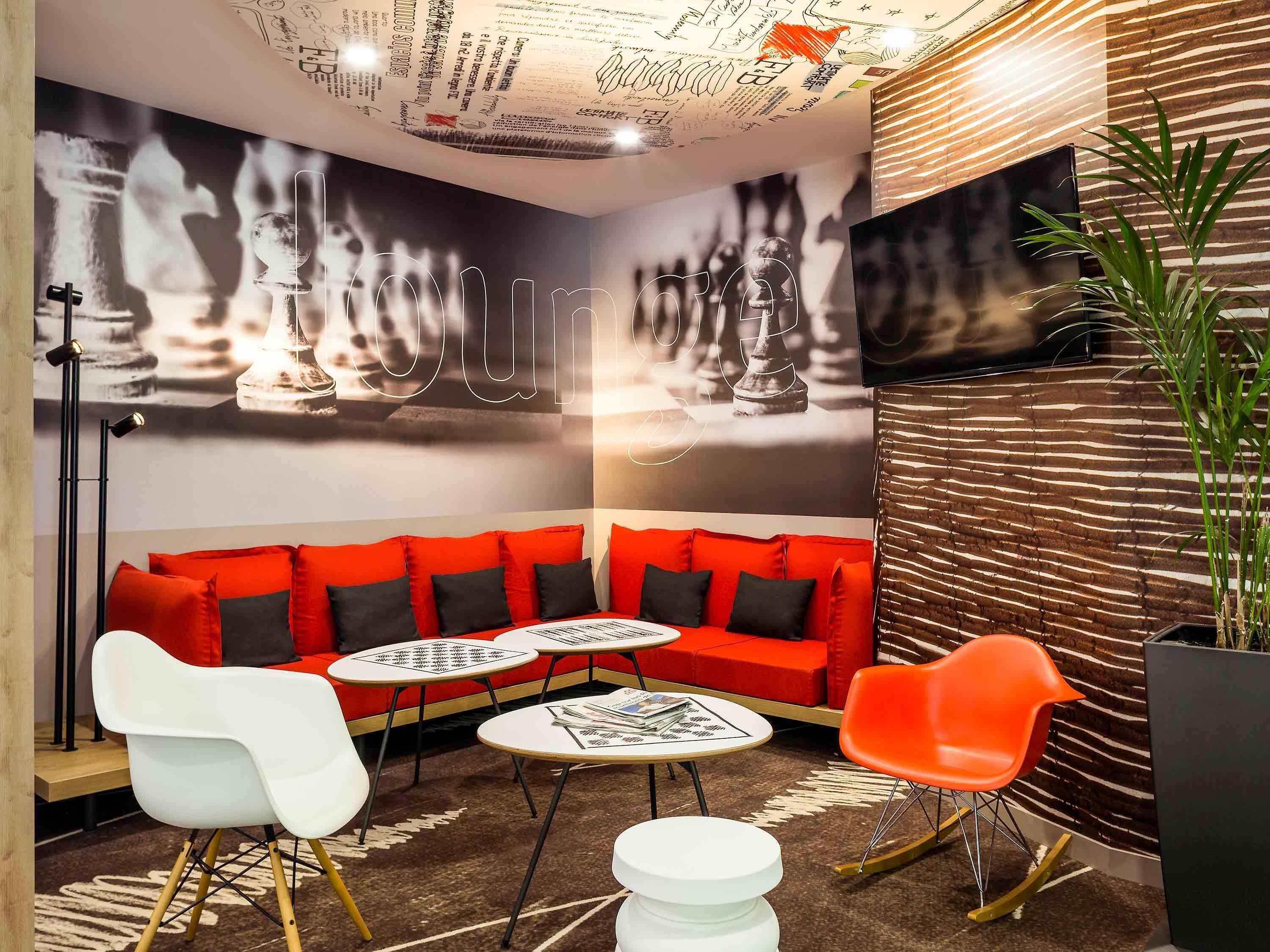 Un espace détente moderne avec un canapé rouge, des fauteuils blancs et orange, et une petite table.