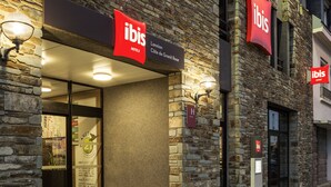 Exterior d'un hotel amb façana de pedra, senyalització 'ibis' i entrada de vidre.