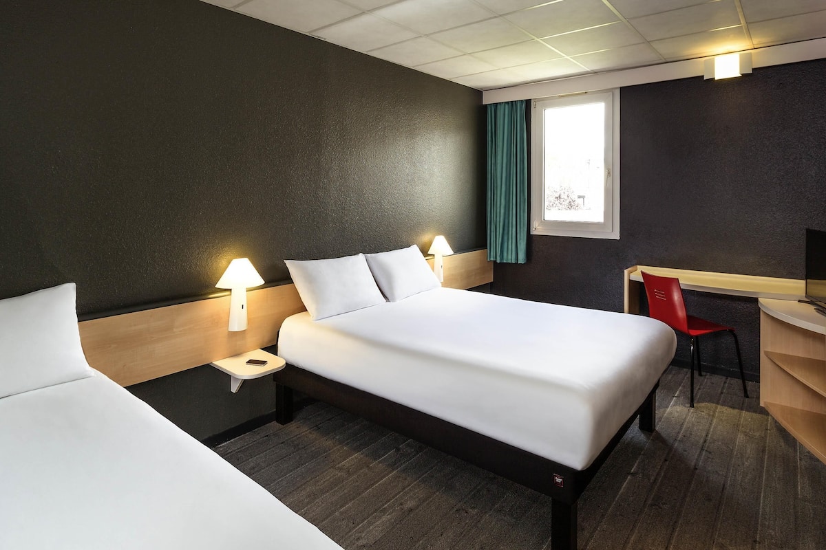 Habitación de hotel con dos camas, un escritorio, una silla y un televisor.