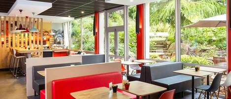 Un café moderno con asientos rojos y grises, amplias ventanas que dan a zonas verdes y un diseño de techo elegante.