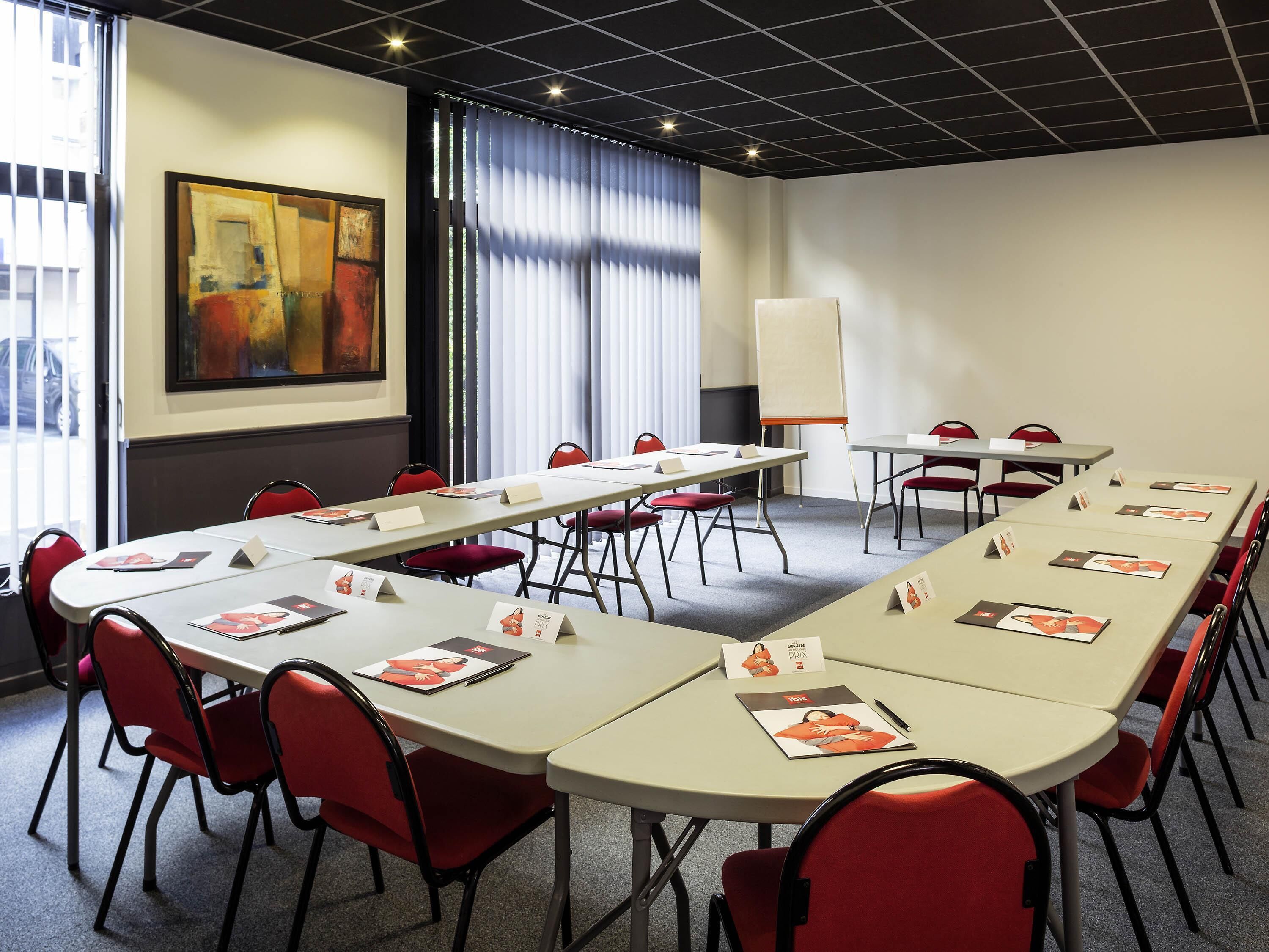 A conference room with a long table, red chairs, a whiteboard, and a painting on the wall.
