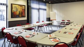 A conference room with a long table, red chairs, a whiteboard, and a painting on the wall.