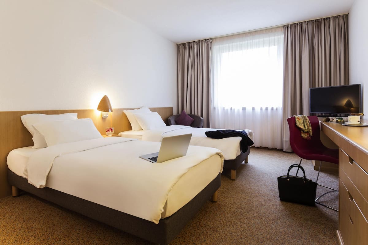 Une chambre d’hôtel avec deux lits, un bureau avec une télévision, une chaise et une lampe de bureau.