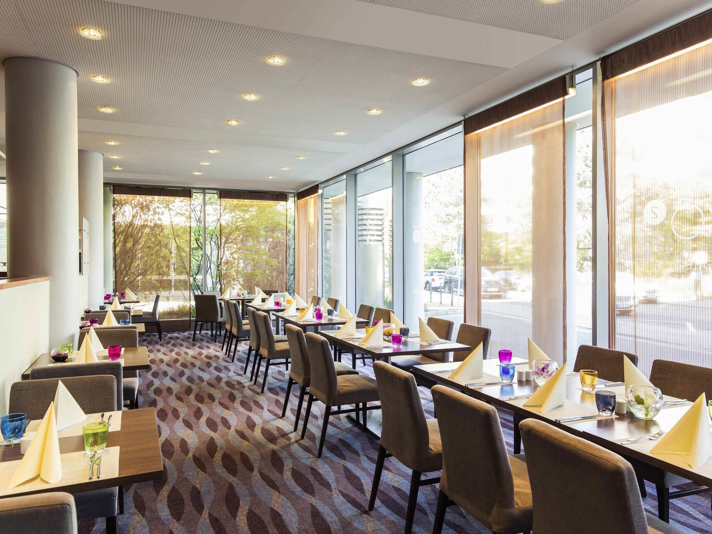 A hotel dining area with long tables, chairs, and large windows.