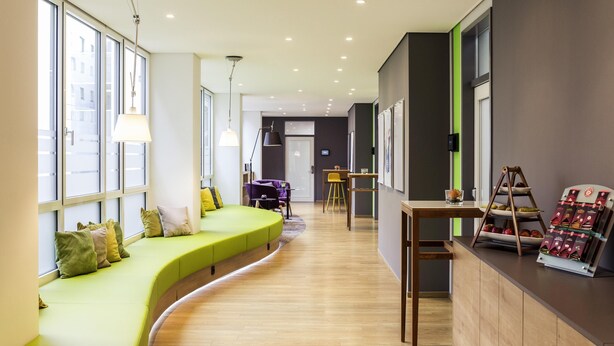 Un interior moderno con una zona de estar verde y curvada, suelo de madera y una recepción con exhibición de objetos.