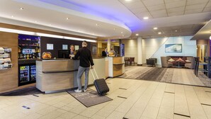 Zona de recepción de hotel con mostrador, área de descanso y pantalla de televisión.