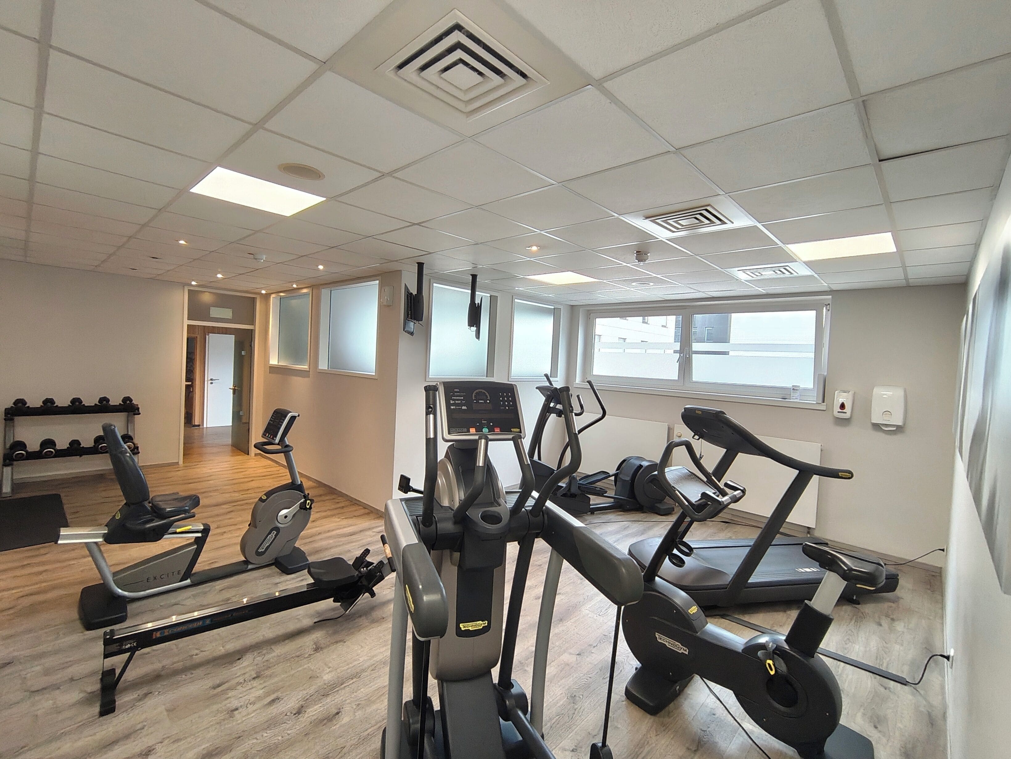 A gym with multiple treadmills, a rowing machine, and dumbbells on racks.