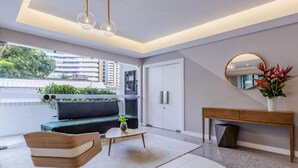 En moderne stue med sofa, sofabord, stol, rundt spejl og et konsolbord med en vase blomster.