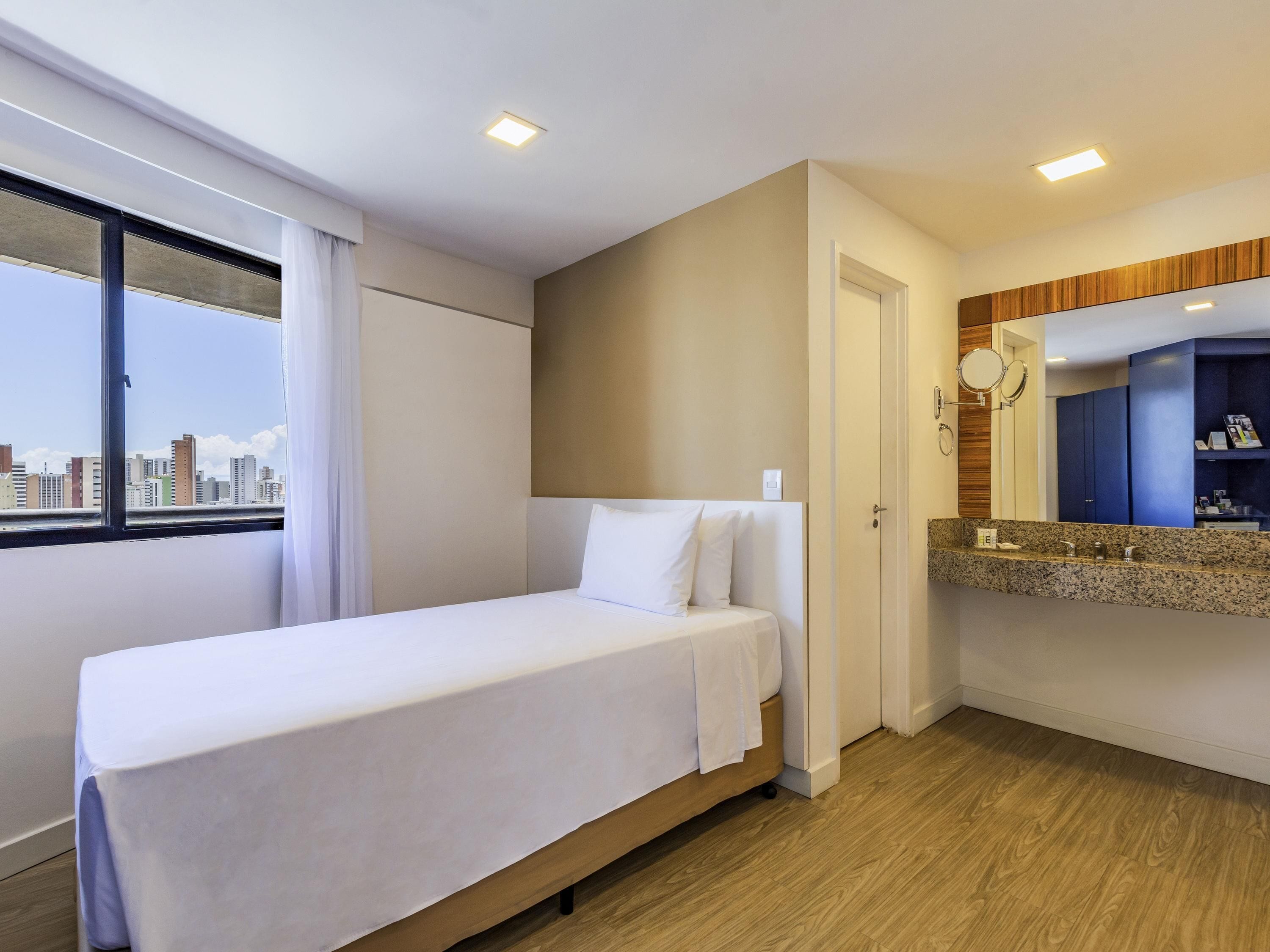 Hotelkamer met een bed, een badkamer met spiegel en uitzicht op de stad.
