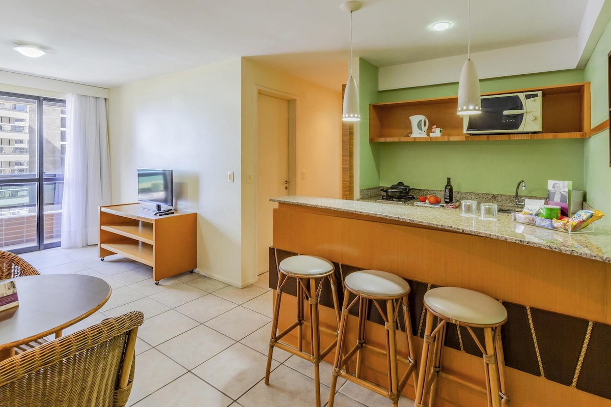 A modern kitchen with a bar area, a dining table with chairs, and a television in a corner.