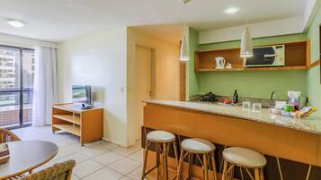 Cozinha moderna com área de bar, mesa de jantar com cadeiras e uma televisão num canto.