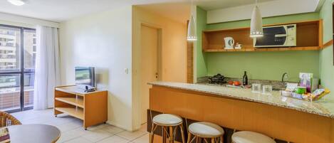 A modern kitchen with a bar area, a dining table with chairs, and a television in a corner.