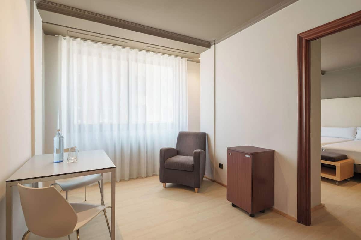 A hotel room with a bed, a chair, a desk, a wardrobe, and a window with curtains.