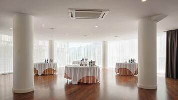 A spacious room with two round tables, white drapery, and large windows.