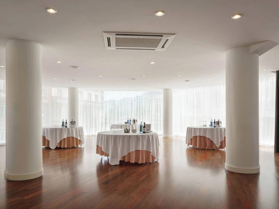 A spacious room with two round tables, white drapery, and large windows.