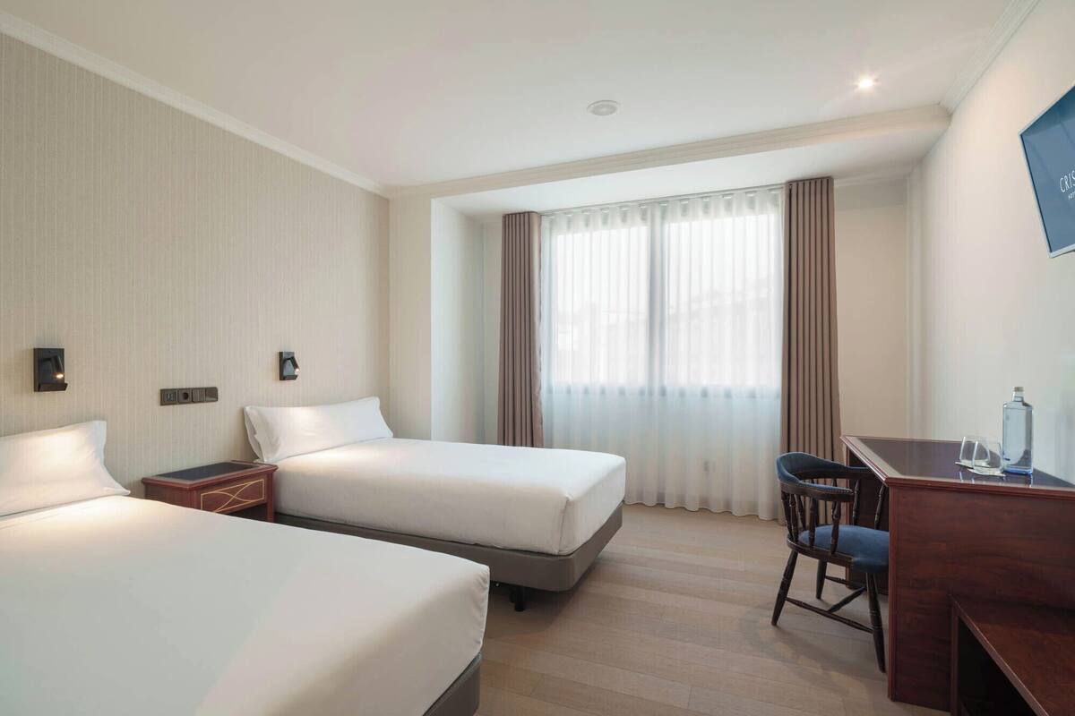 A hotel room with two beds, a desk, a chair, and a TV.