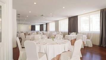 Un salón de banquetes con mesas redondas, sillas blancas y un techo alto con iluminación empotrada.