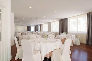 A banquet hall with round tables, white chairs, and a high ceiling with recessed lighting.