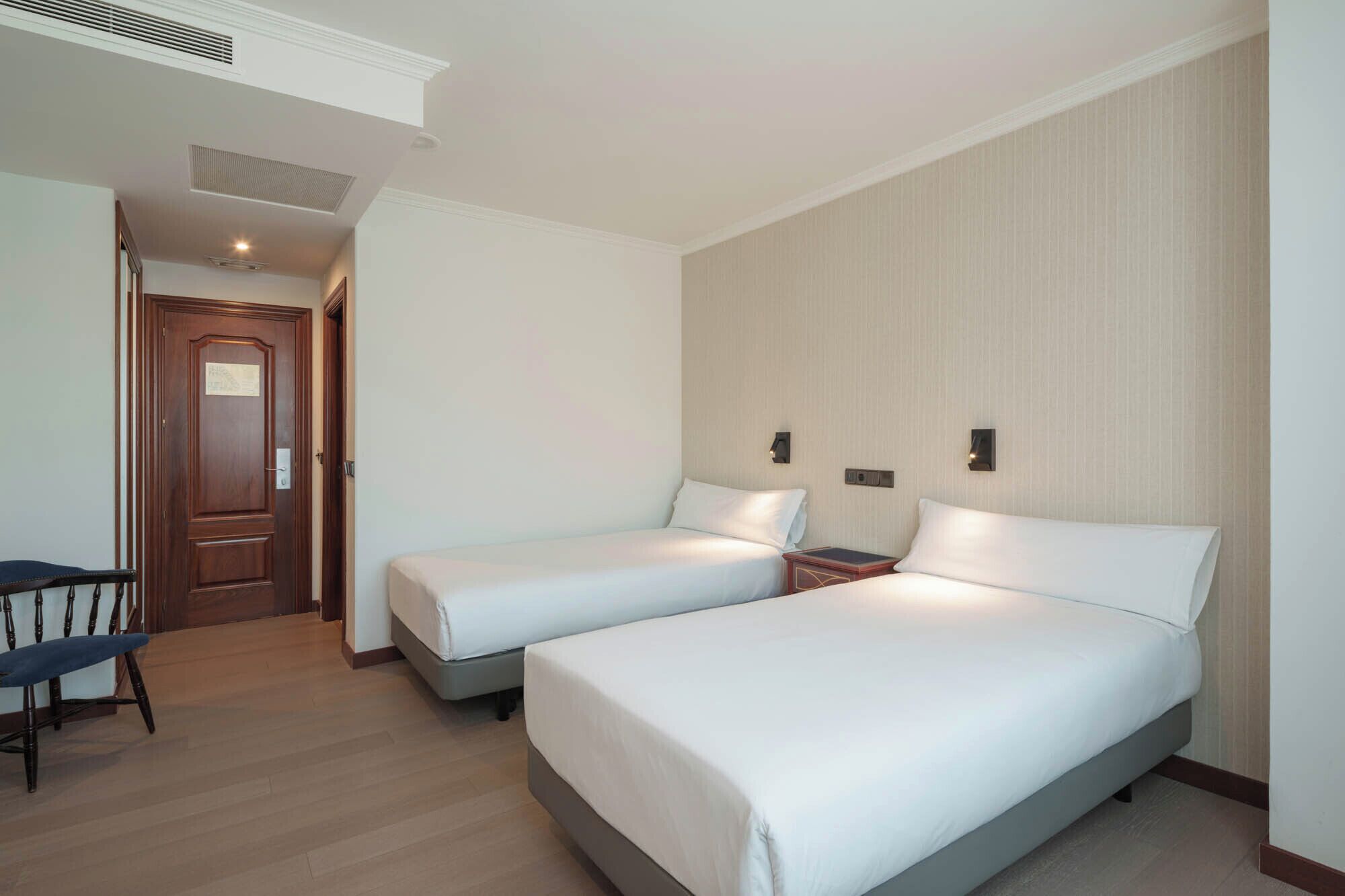 A hotel room with two single beds, a desk, and a chair.