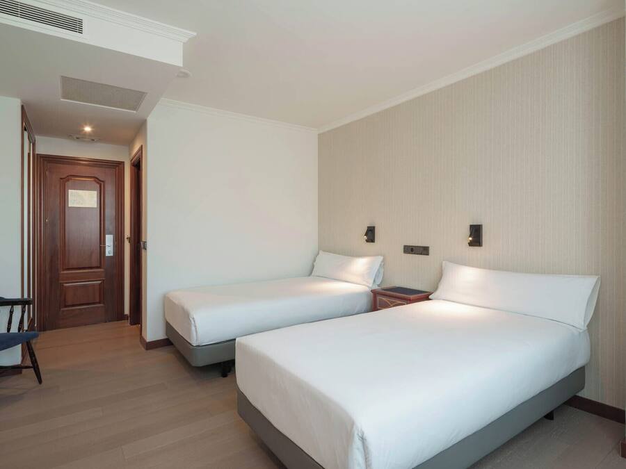 A hotel room with two single beds, a desk, and a chair.