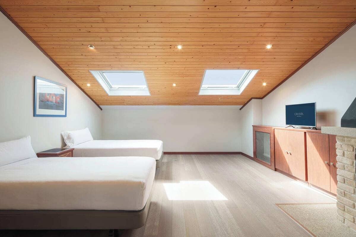 A modern room with two beds, skylights, a television, and a brick wall.