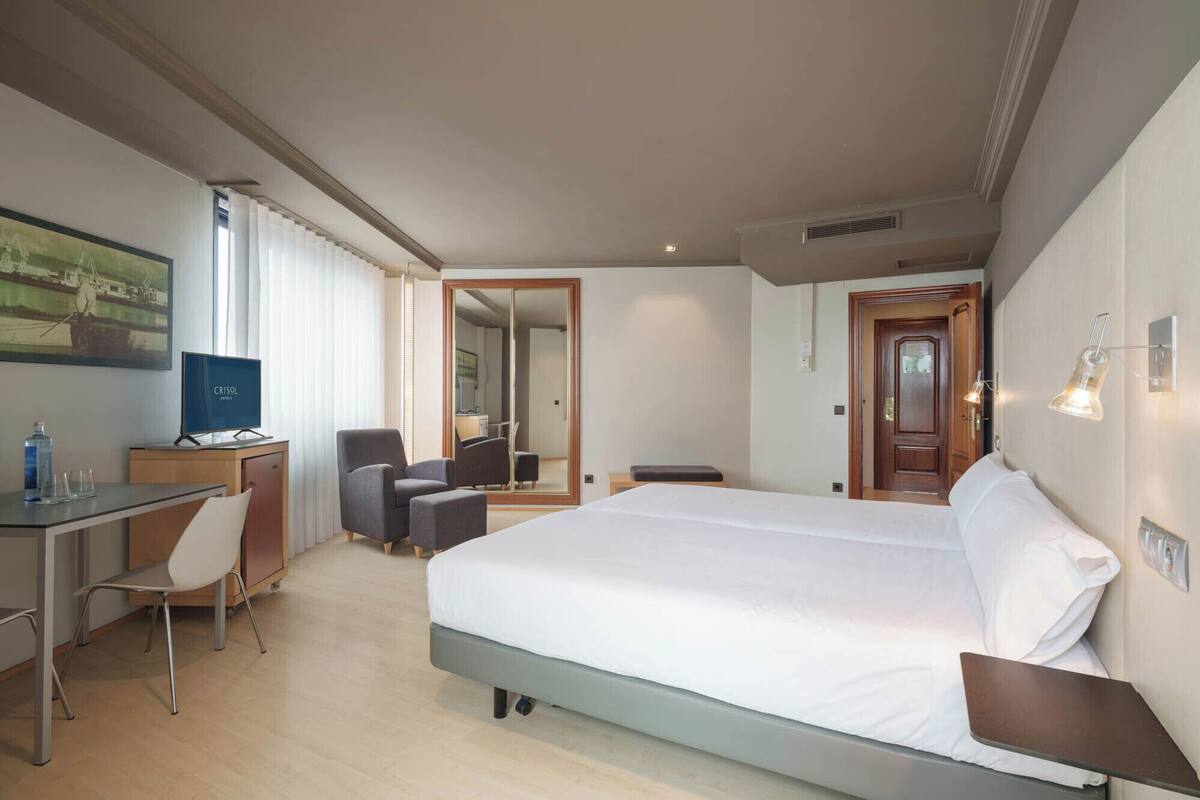 A hotel room with a bed, desk, chairs, and a television.