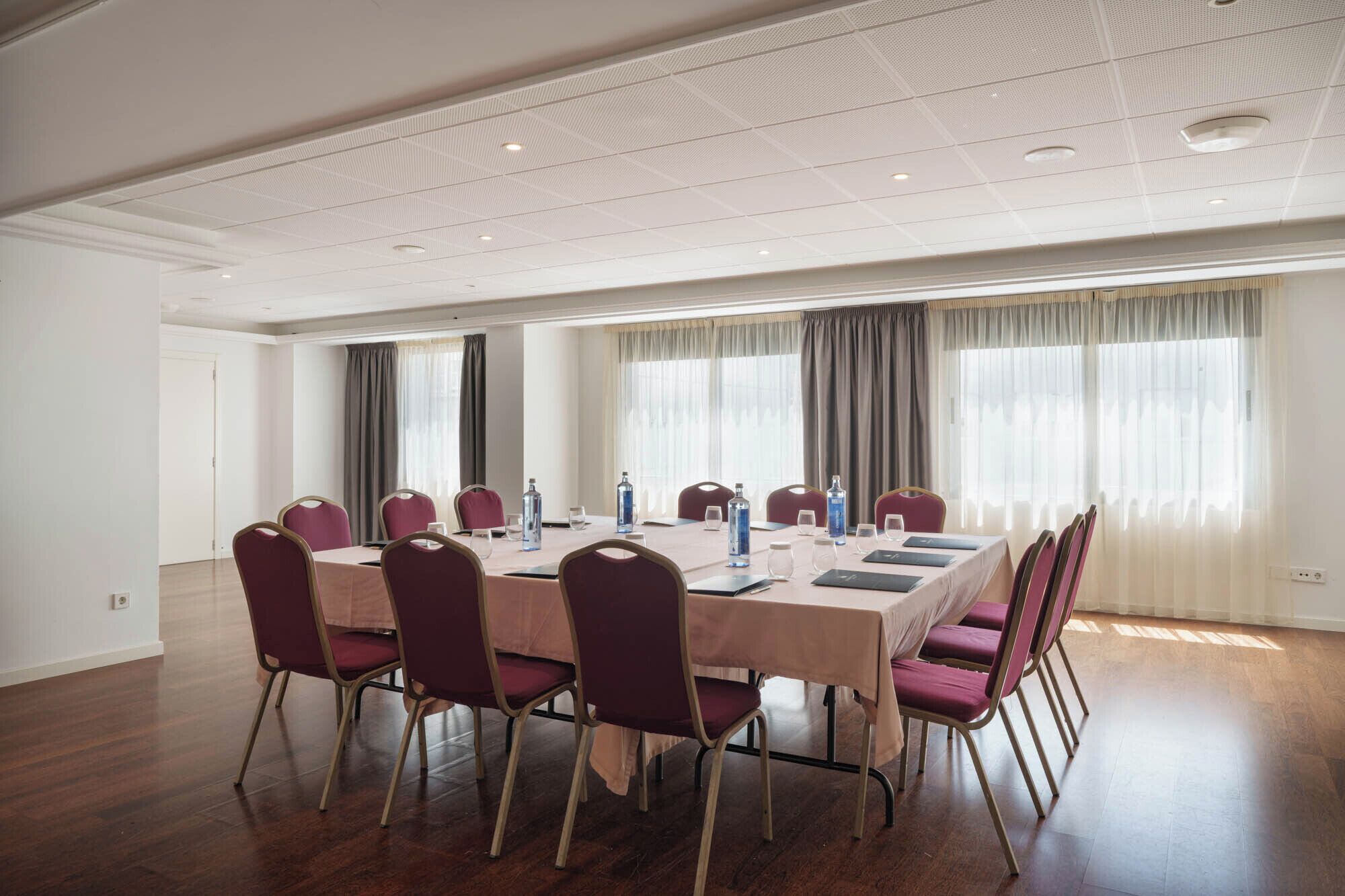 A conference room with a long table, chairs, and windows with curtains.