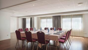 A conference room with a long table, chairs, and windows with curtains.