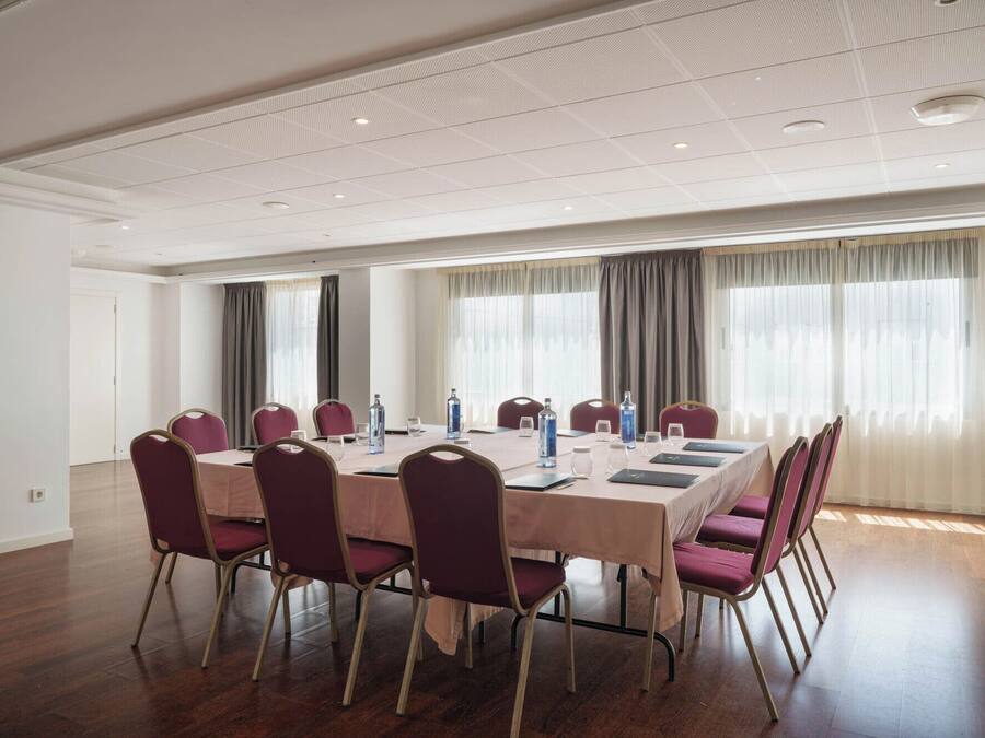 A conference room with a long table, chairs, and windows with curtains.