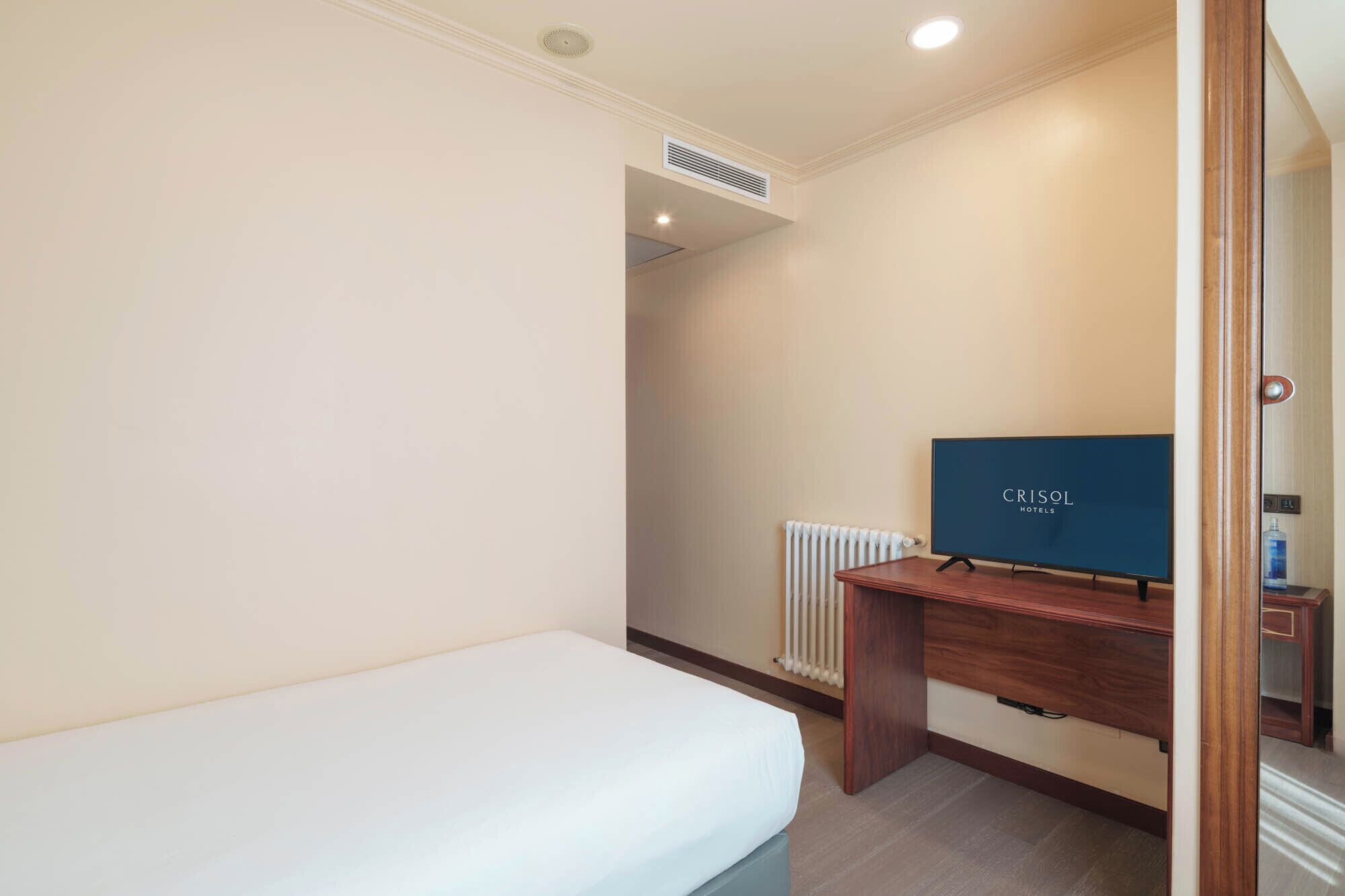 Une chambre d’hôtel avec un lit simple, un bureau en bois, une télévision et un radiateur.