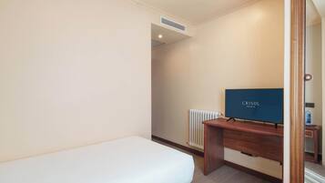 Une chambre d’hôtel avec un lit simple, un bureau en bois, une télévision et un radiateur.