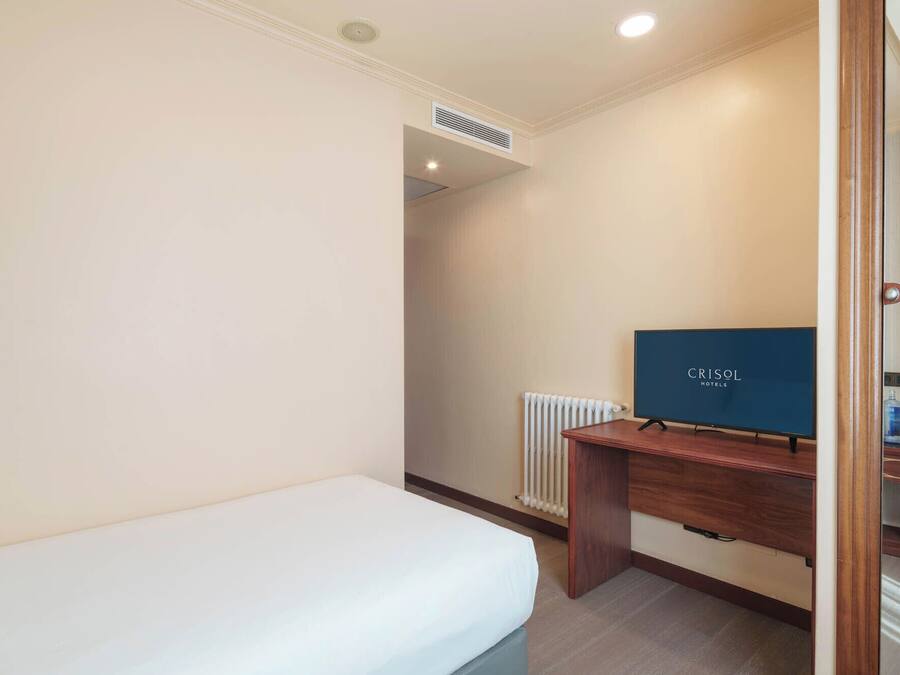 Habitació d'hotel amb un llit individual, un escriptori de fusta, una televisió i un radiador.