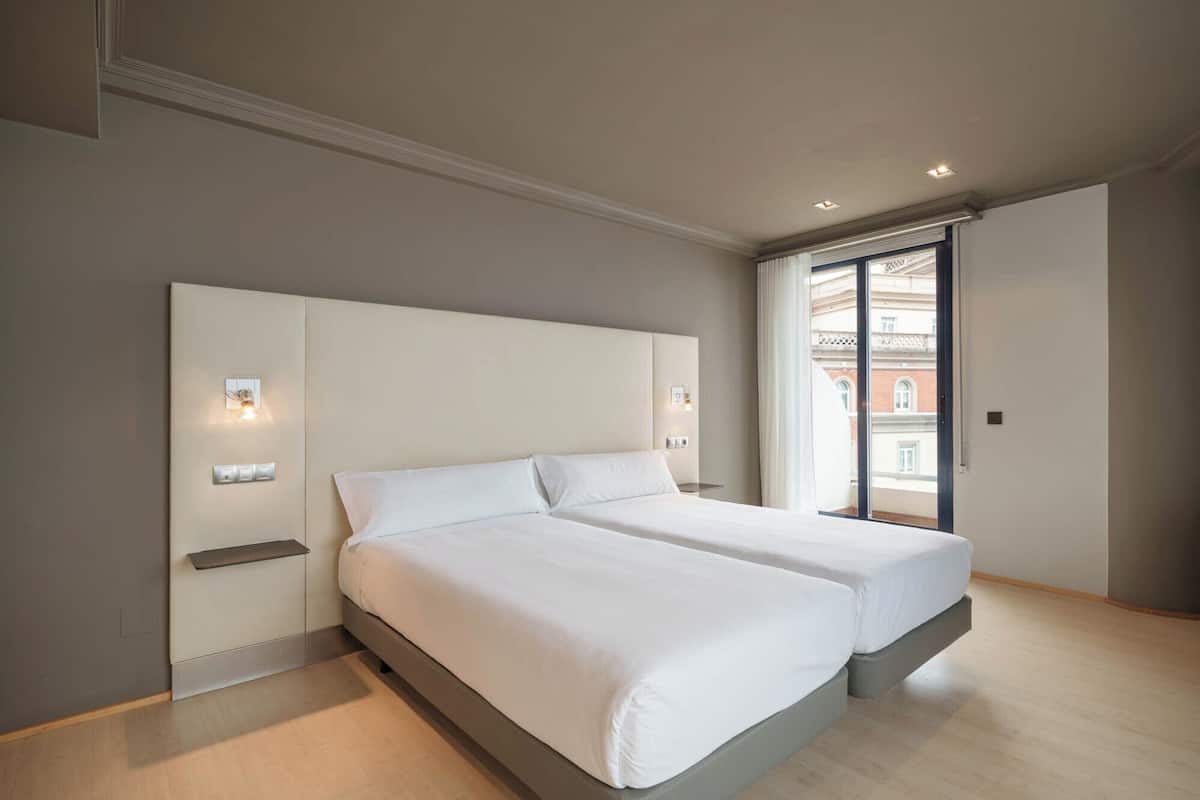 A modern bedroom with a large bed, bedside tables, and a view of a building through a window.