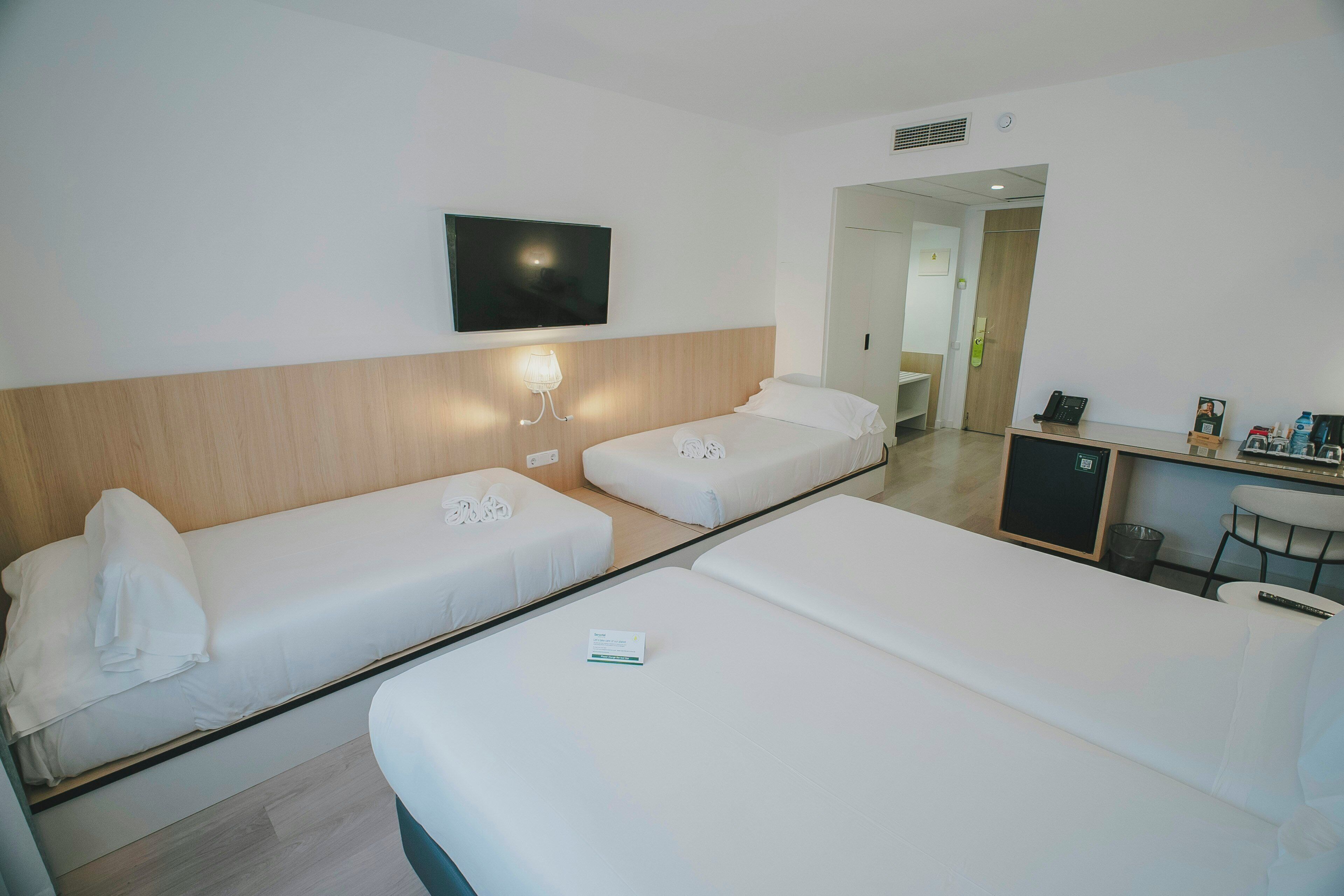 A hotel room with two single beds, a desk, a chair, a TV, and a mirror.