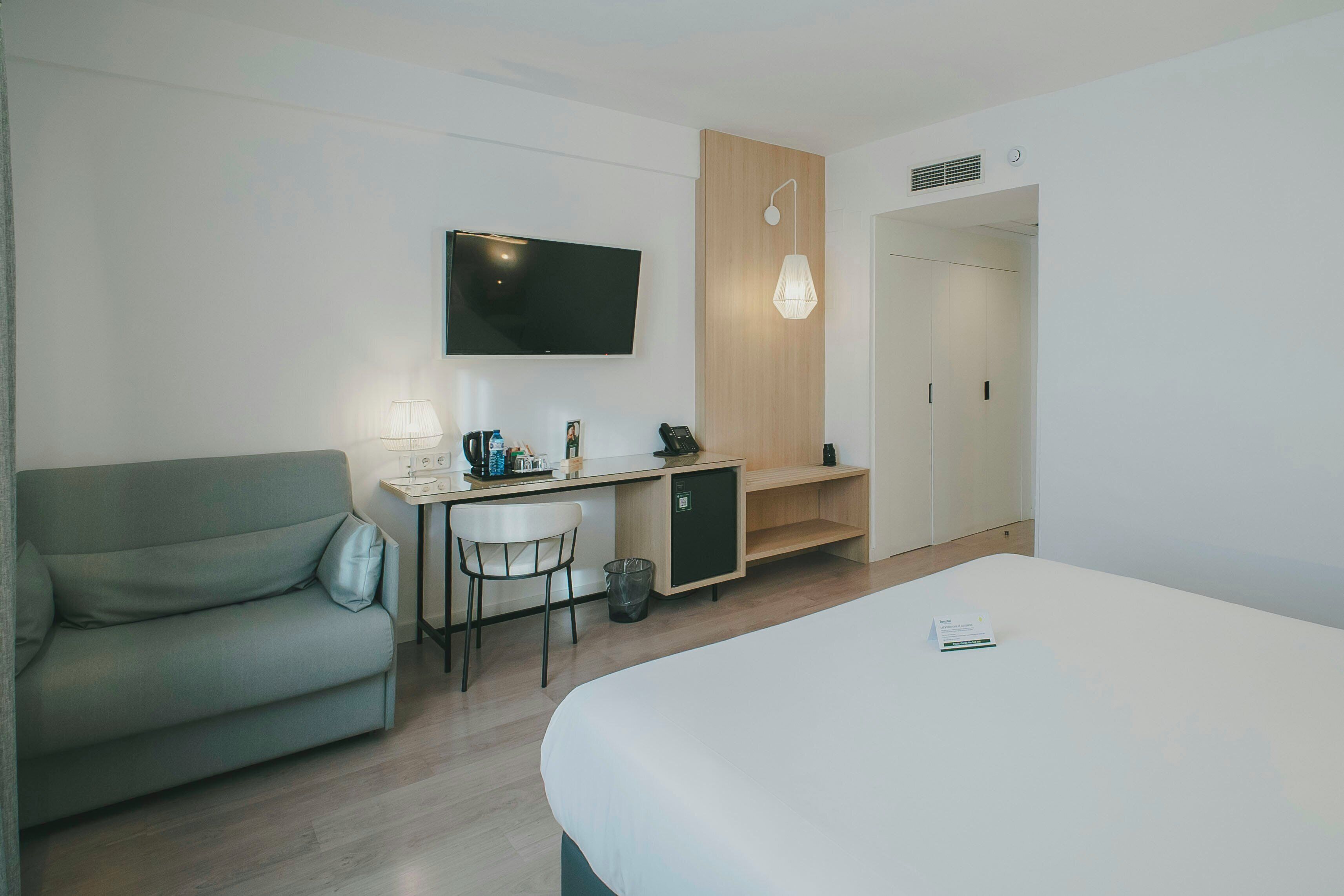 Una habitación de hotel moderna con una cama, un escritorio con una silla, un televisor y una pared de paneles de madera.