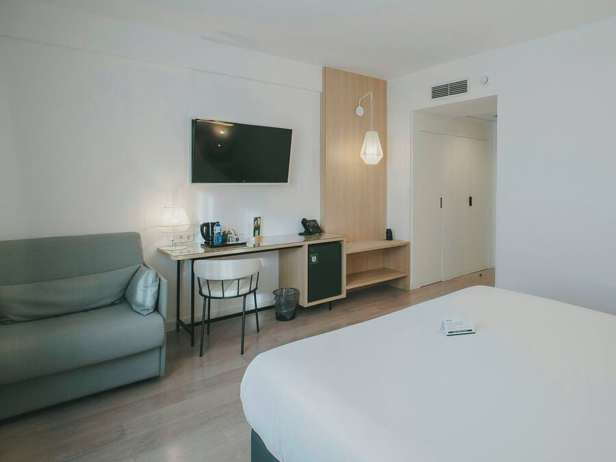 Una habitación de hotel moderna con una cama, un escritorio con una silla, un televisor y una pared de paneles de madera.