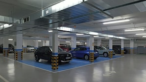 Un estacionamiento de varios niveles con automóviles estacionados en espacios designados, columnas estructurales visibles e iluminación colgante.