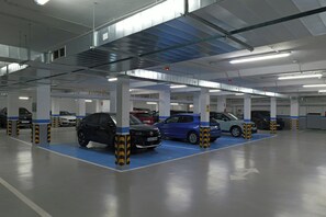 A multi-level parking garage with cars parked in designated spaces, visible structural columns, and overhead lighting. - Hotel Sercotel Carlos III (Cartagena)