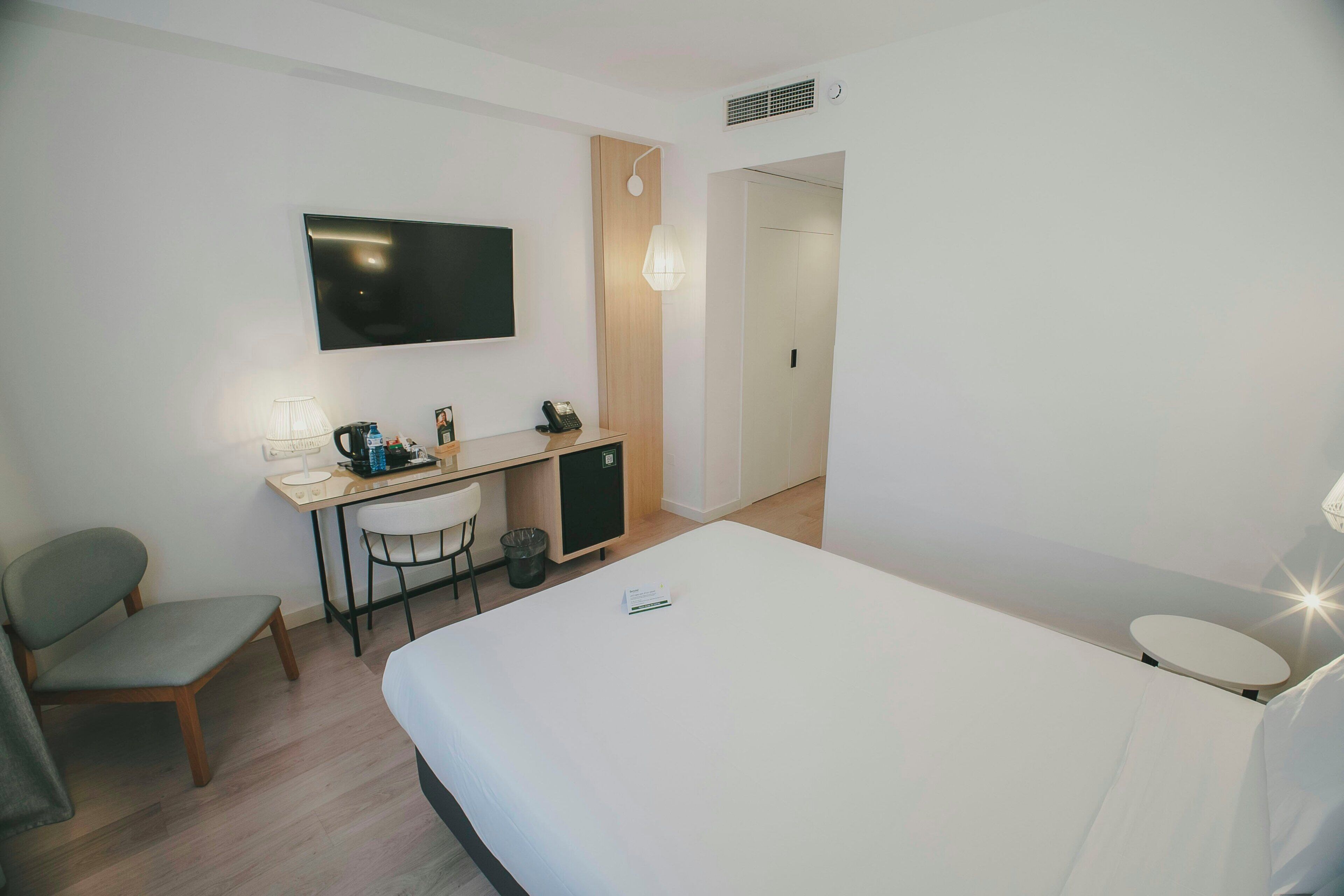 A hotel room with a bed, a desk with a chair, a television, and a small cabinet.