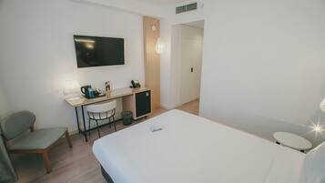 A hotel room with a bed, a desk with a chair, a television, and a small cabinet.