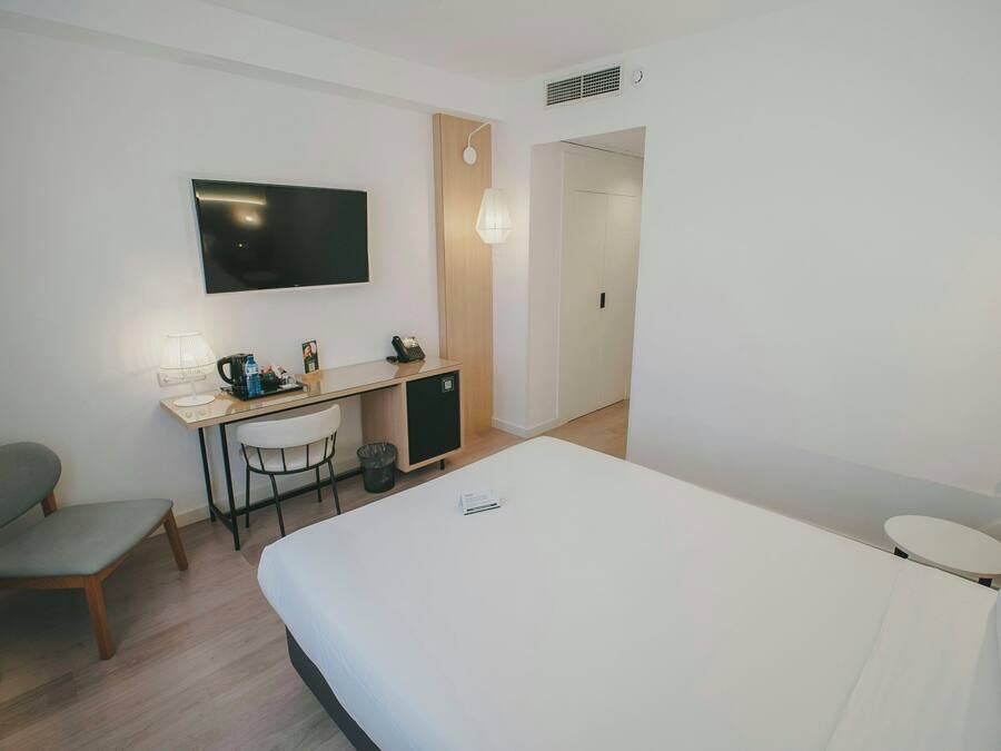 A hotel room with a bed, a desk with a chair, a television, and a small cabinet.