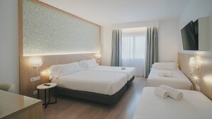 Habitación de hotel con dos camas, un escritorio, un televisor y un ventanal con cortinas.