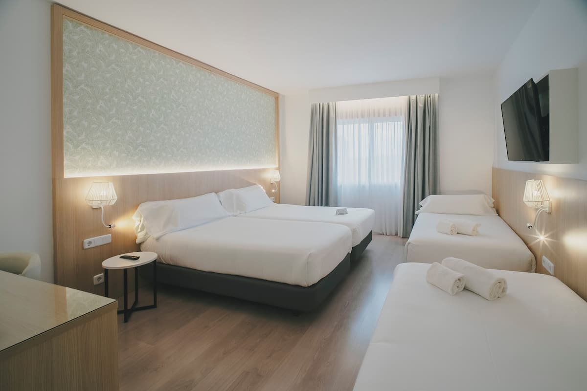 Ein Hotelzimmer mit zwei Betten, einem Schreibtisch, einem Fernseher und einem großen Fenster mit Vorhängen.