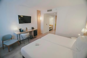 Ein Hotelzimmer mit Bett, Schreibtisch, Stuhl, Fernseher und einem durch eine offene Tür einsehbaren Badezimmer.