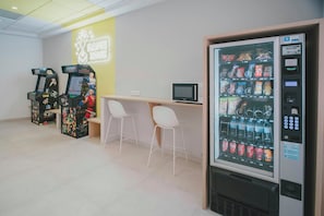 Ein Spielbereich mit Spielautomaten, einem Verkaufsautomaten und einem kleinen Schreibtisch mit Stühlen.