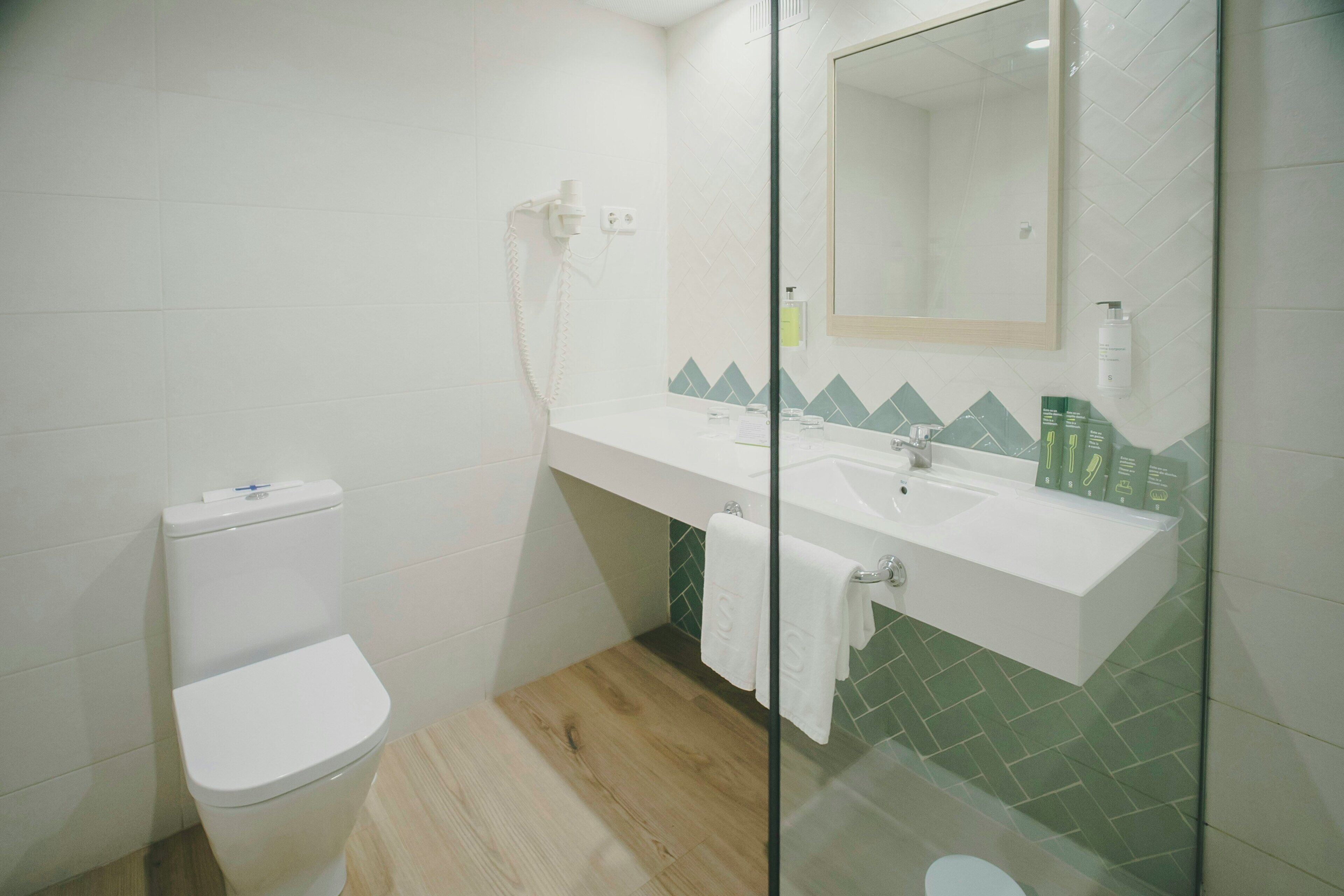 A bathroom with a toilet, a sink, a glass shower enclosure, and a mirror.